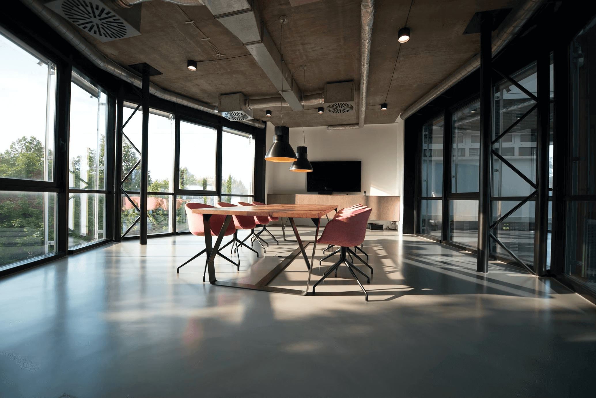 Industrial interior view of a boardroom, floor to ceiling windows, exposed duct work, rose pink chairs